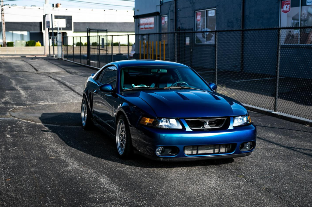 A sleek Ford Mustang SVT Cobra with a chameleon-style vinyl wrap reflecting shades of green, purple, and blue.