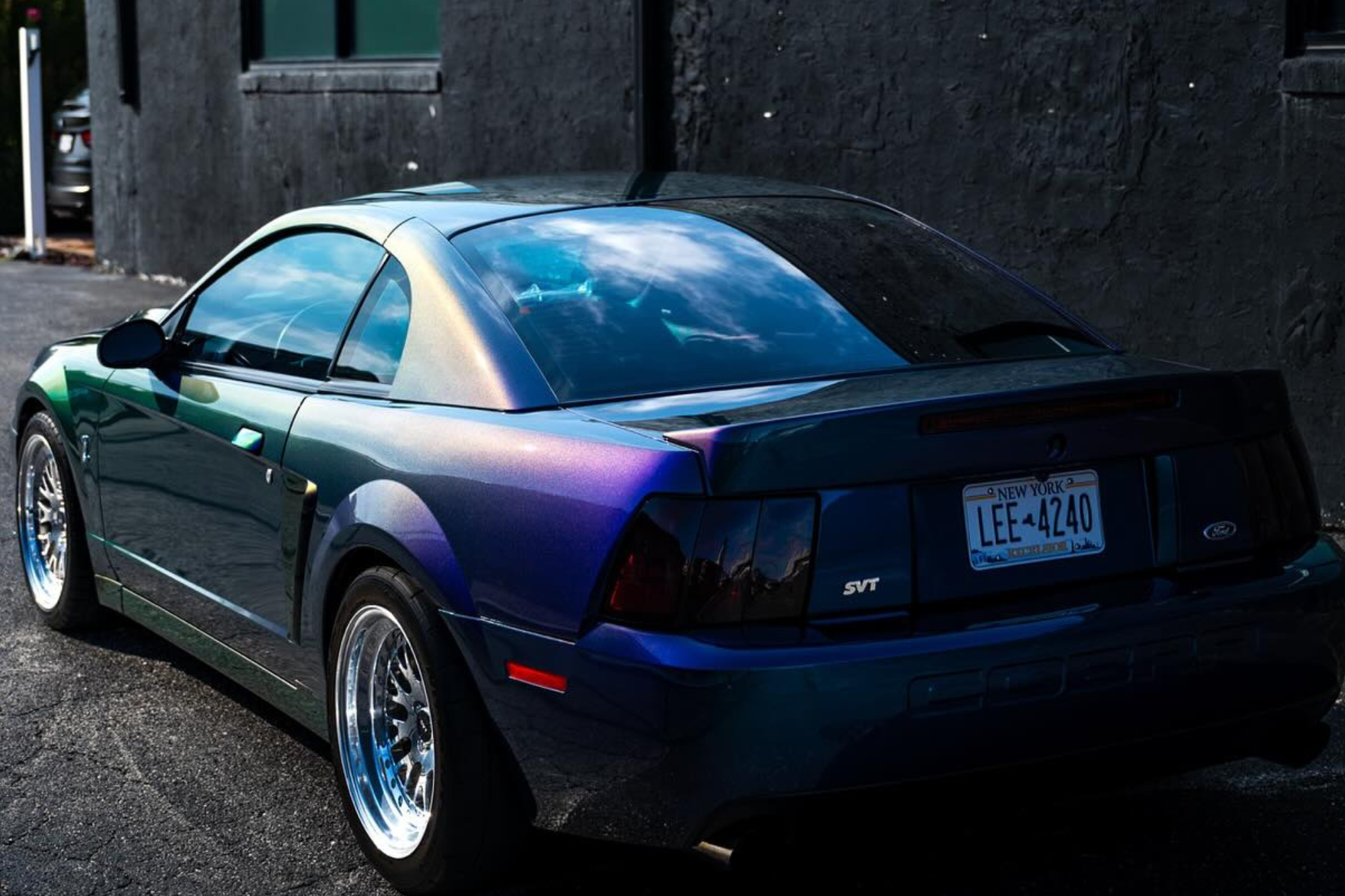 A sleek Ford Mustang SVT Cobra with a chameleon-style vinyl wrap reflecting shades of green, purple, and blue.